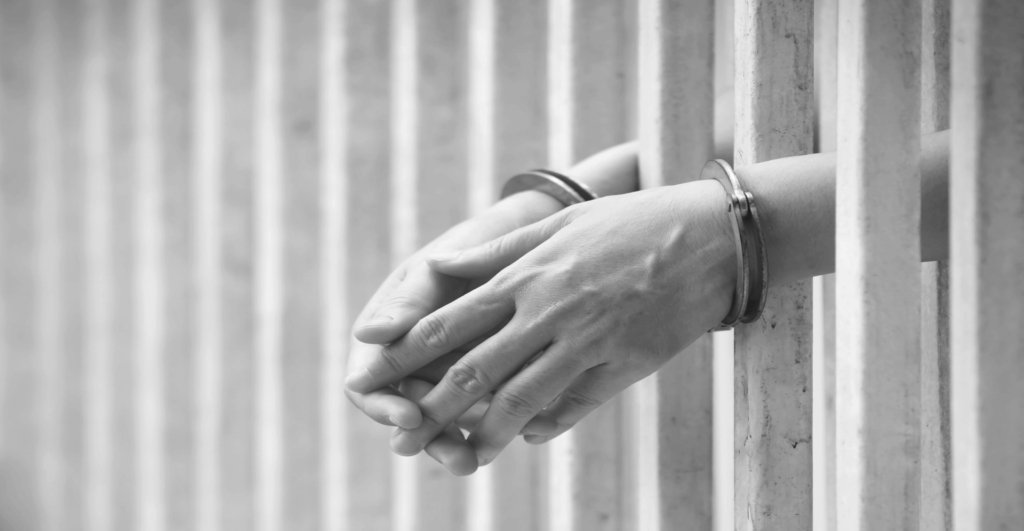 This image of handcuffed hands outside a wall of cell bars illustrates the defence and enforcement side of fake shops and fake websites.