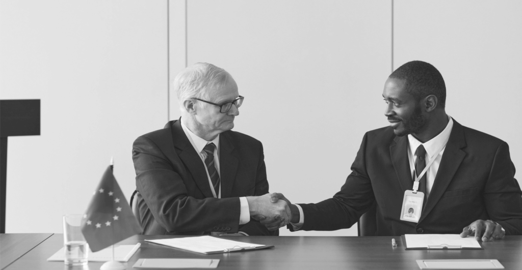 This image of two people shaking hands in front of the EU flag illustrates our discussion topic: NIS2, the changes for your organization, and the relevance of Corporate Domain Management.
