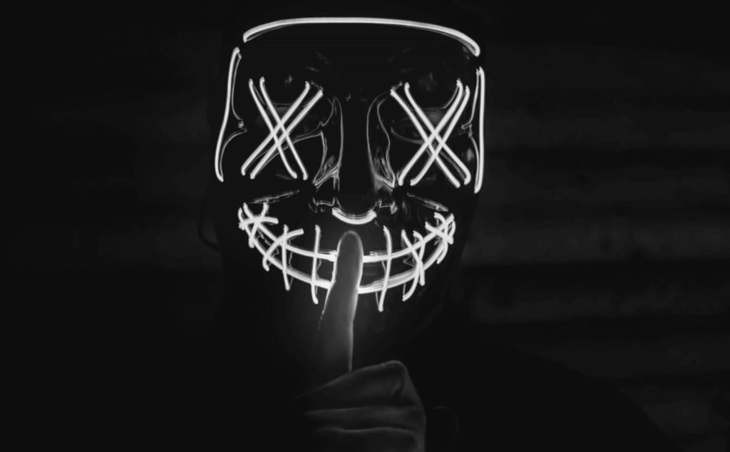 This image of a masked figure performing a "shushing" gesture illustrates this article's topic: understanding phishing domain impersonation tactics, specifically the topic of sound squatting.