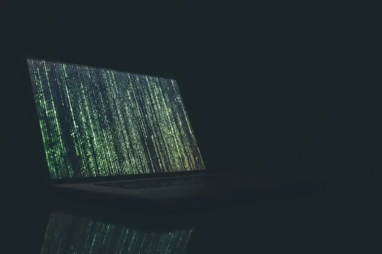 Laptop screen displaying green code in a dark environment, symbolizing cybersecurity or hacking activity